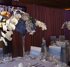 Высокие настольные композиции на столы гостей — Свадебное оформление ресторана. Высокие цветочные композиции в вазах-мартинницах. Сине-бело-голубая гамма. Белые орхидеи фаленопсис, голубая и синяя гортензия.